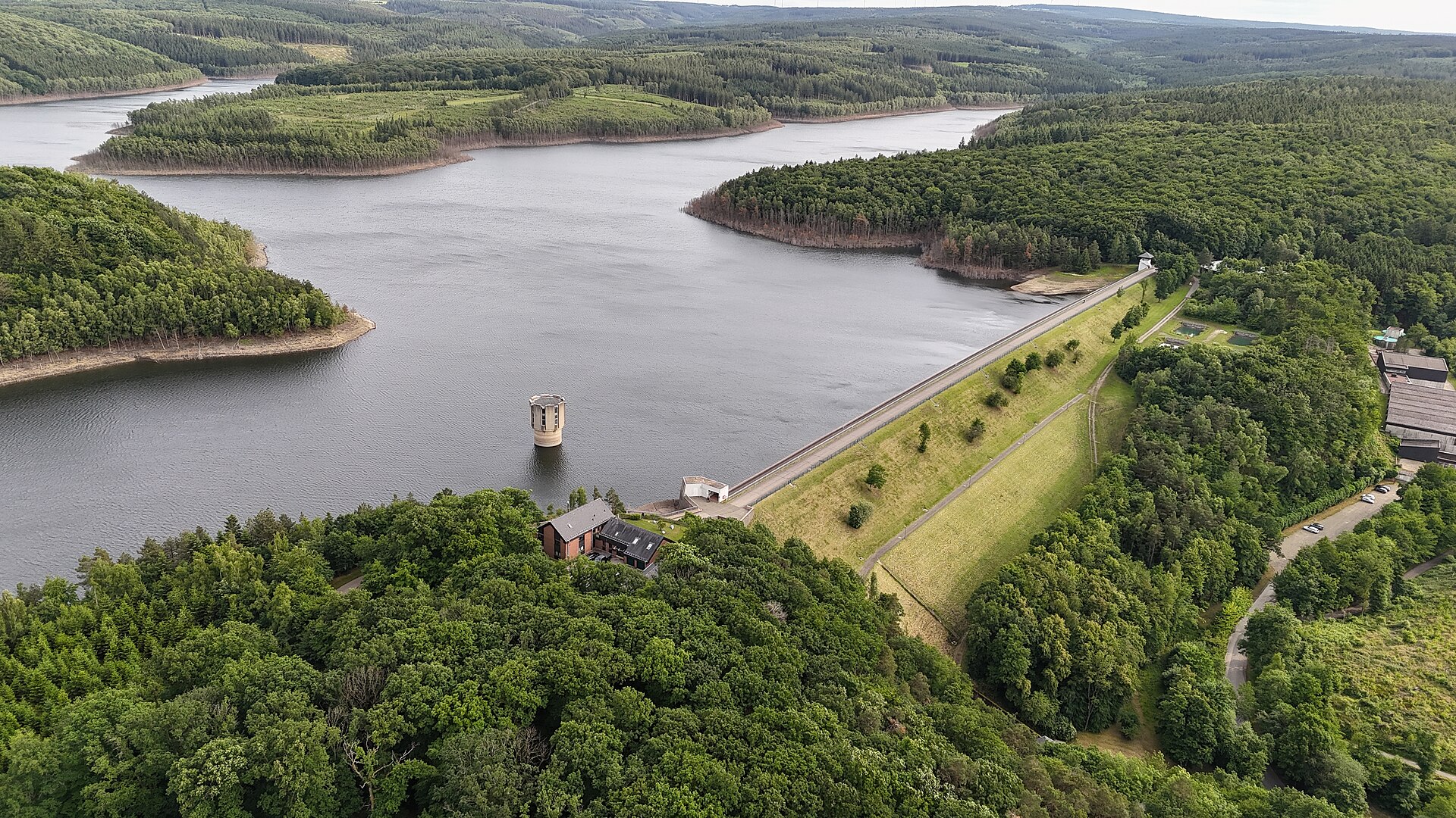 Luftaufnahme der Wehebachtalsperre mit begrüntem Staudamm, Entnahmeturm und dem von Wald umgebenen See.
