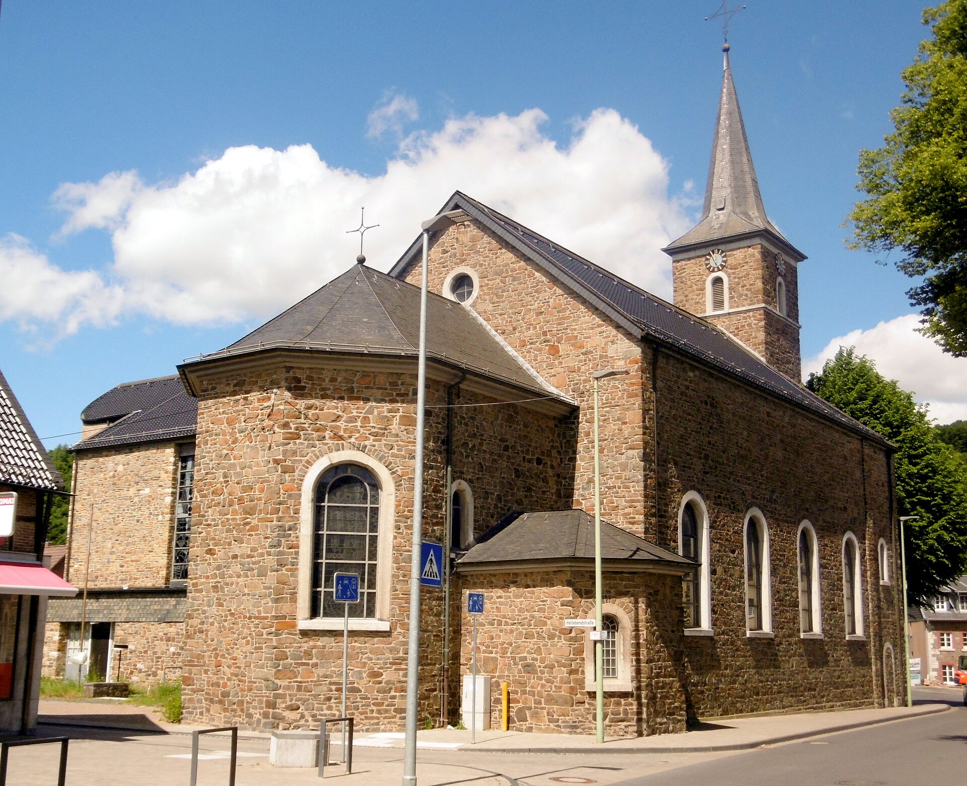 Die Bruchsteinkirche St. Rochus in Zweifall mit Spitzturm unter blauem Himmel.